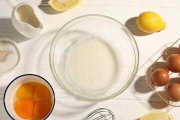Whisk, egg whites in bowl, eggs and other products on white wooden table, flat lay