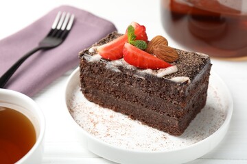 Piece of delicious chocolate cake with strawberry, almonds and tea on white wooden table, closeup