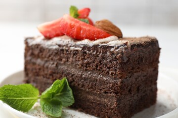 Piece of delicious chocolate cake with strawberry, almonds and mint on table, closeup
