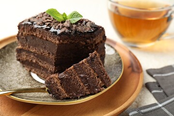 Piece of delicious chocolate cake with mint and tea on table, closeup