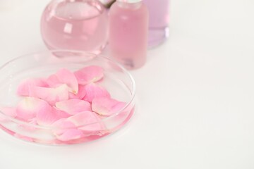 Making luxury perfume. Essential oils in glassware and flowers on white table, closeup. Space for text