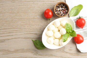 Tasty mozzarella cheese balls, tomatoes, basil and peppercorns on wooden table, flat lay. Space for text