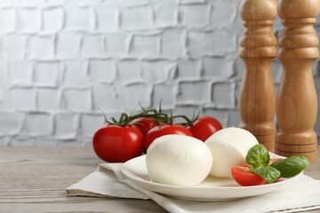 Tasty mozzarella cheese balls, tomatoes and basil on wooden table, closeup. Space for text