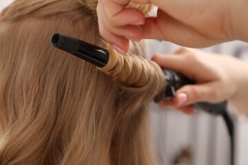 Naklejka premium Hairdresser curling woman's hair in salon, closeup