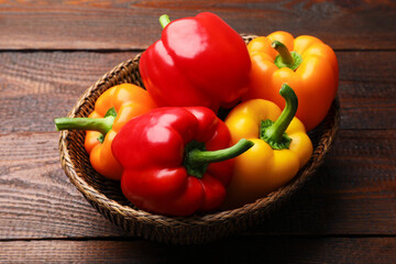 Fresh colorful bell peppers in wicker basket on wooden table, closeup