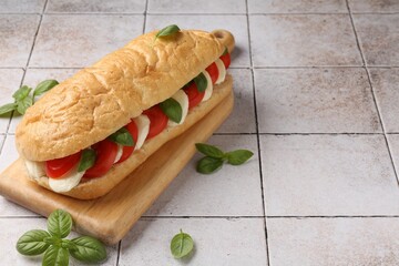 Tasty sandwich with mozzarella cheese, tomatoes and basil on light tiled table, closeup. Space for text