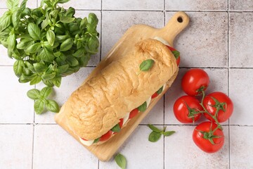 Tasty sandwich with mozzarella cheese, tomatoes and basil on light tiled table, flat lay
