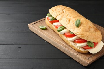 Tasty sandwich with mozzarella cheese, tomatoes and basil on black wooden table, closeup