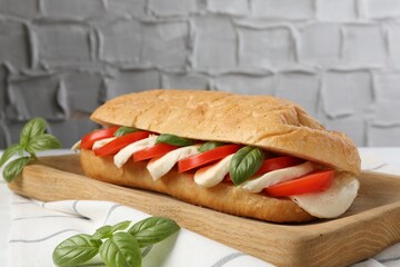 Tasty sandwich with mozzarella cheese, tomatoes and basil on table against grey textured wall, closeup