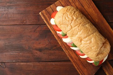 Tasty sandwich with mozzarella cheese, tomatoes and basil on wooden table, top view. Space for text