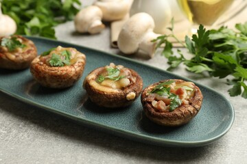Delicious stuffed mushrooms with melted cheese and parsley on grey textured table, closeup