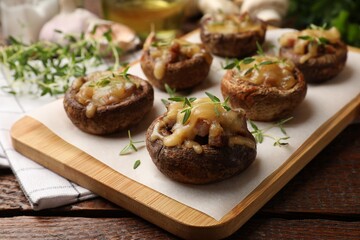 Delicious stuffed mushrooms with melted cheese and thyme on wooden table, closeup