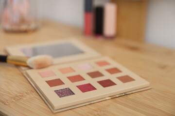Eyeshadow palette with brush on wooden dressing table indoors, closeup. Cosmetic products