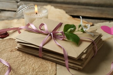 Stack of love letters, flower, candle and parchment sheets on wooden table, closeup
