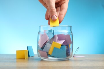 Woman taking paper with message out of jar at wooden table, closeup