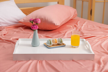 Tray with delicious breakfast and flowers on bed indoors
