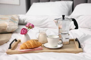 Tray with delicious breakfast and flowers on bed indoors, closeup