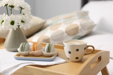 Tray with delicious breakfast and flowers on bed indoors, closeup