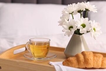 Tray with delicious breakfast and flowers on bed indoors, closeup