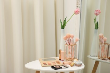 Different makeup products and brushes on white table near mirror indoors. Space for text
