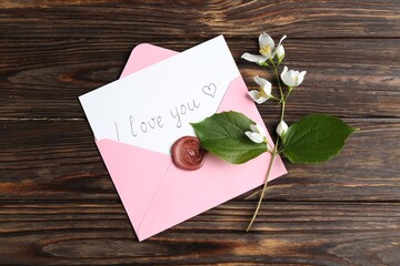 Letter with phrase I Love You, envelope and beautiful flowers on wooden table, flat lay