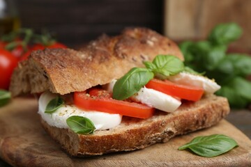 Tasty sandwich with mozzarella cheese, tomatoes and basil on wooden table, closeup