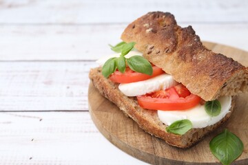 Tasty sandwich with mozzarella cheese, tomatoes and basil on white wooden table, closeup. Space for text