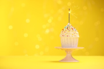 Burning sparkler in cupcake, sprinkles and stand on yellow background with blurred lights, space for text