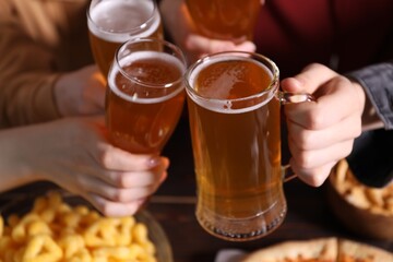 Friends clinking glasses of beer at table, closeup
