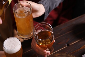 Pouring beer into woman's glass at wooden table, closeup