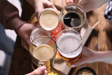 Friends clinking glasses of beer at table, closeup