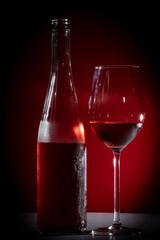 bottle and glass of rosé wine with a red background and side lighting
