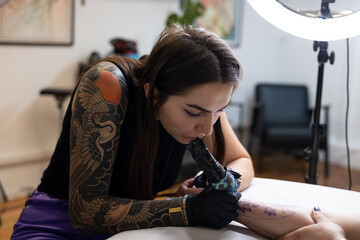 Close-up of a tattoo artist creating a floral tattoo on a woman's hand using a tattoo machine in...