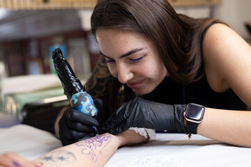 Close-up of a tattoo artist creating a floral tattoo on a woman's hand using a tattoo machine in...