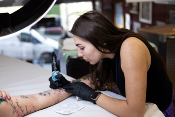 Close-up of a tattoo artist creating a floral tattoo on a woman's hand using a tattoo machine in...
