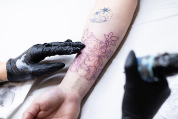 Close-up of a tattoo artist creating a floral tattoo on a woman's hand using a tattoo machine in...