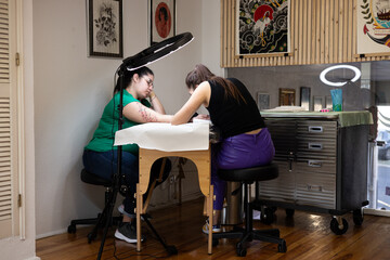 Close-up of a tattoo artist creating a floral tattoo on a woman's hand using a tattoo machine in...