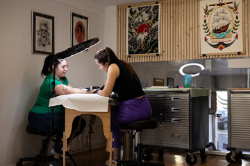 Close-up of a tattoo artist creating a floral tattoo on a woman's hand using a tattoo machine in...