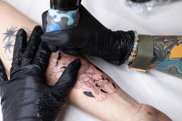 Close-up of a tattoo artist creating a floral tattoo on a woman's hand using a tattoo machine in...