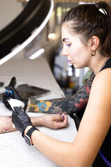 Close-up of a tattoo artist creating a floral tattoo on a woman's hand using a tattoo machine in...