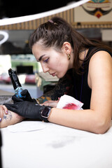 Close-up of a tattoo artist creating a floral tattoo on a woman's hand using a tattoo machine in...