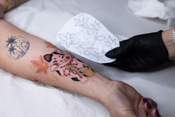 Close-up of a tattoo artist creating a floral tattoo on a woman's hand using a tattoo machine in...