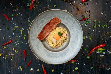 close up of a plate of pasta carbonara with a slice of bacon 