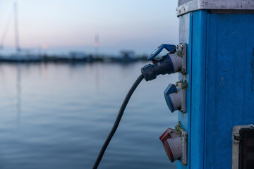 Electric power source connected at a marina during twilight with moored boats and calm water...