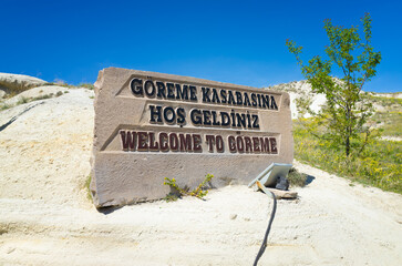 Welcome sign to Goreme in Cappadocia, Turkey. Stone monument with Turkish and English text stands under clear blue sky. Goreme is a very popular travel destination in Türkiye