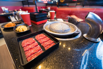 Inside a Korean barbecue restaurant, raw bacon strips are ready to be grilled on a tabletop stove at a dining table