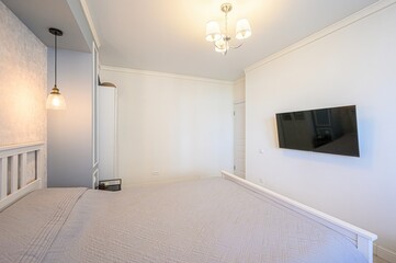 bright, airy bedroom features a white bed with a gray quilt. Pendant lights hang over the headboard, complementing the room's neutral palette and modern style