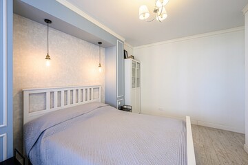 bright, airy bedroom features a white bed with a gray quilt. Pendant lights hang over the headboard, complementing the room's neutral palette and modern style