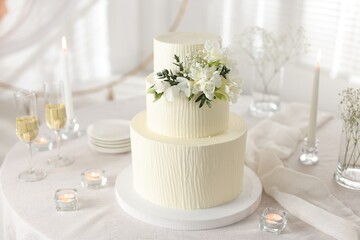 Delicious wedding cake with floral decor and glasses of champagne on table indoors