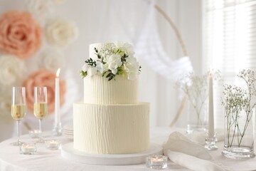 Delicious wedding cake with floral decor and glasses of champagne on table indoors